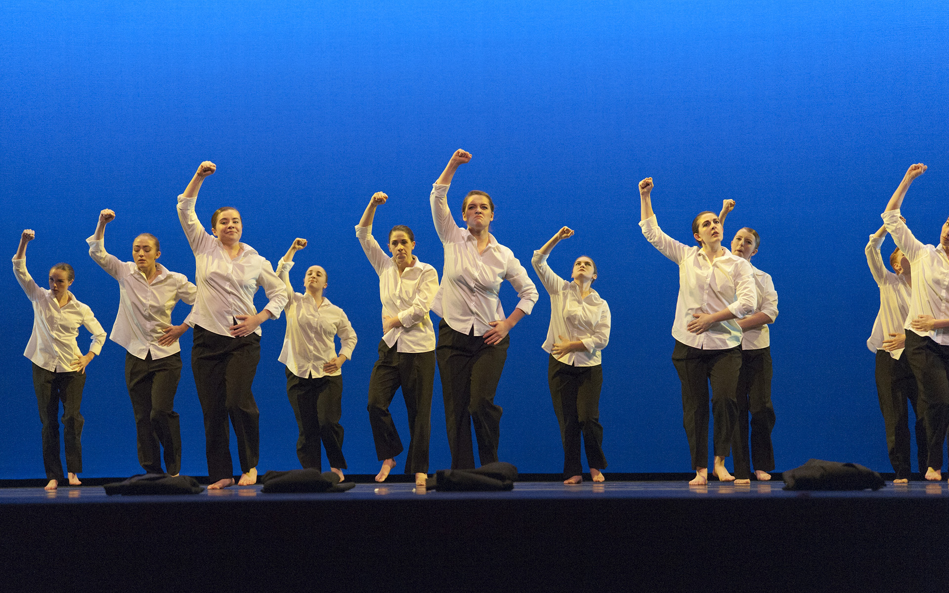 Dance Gala 2017 photo. Female dancers in white dress shirts and black pants, with fists in the air.