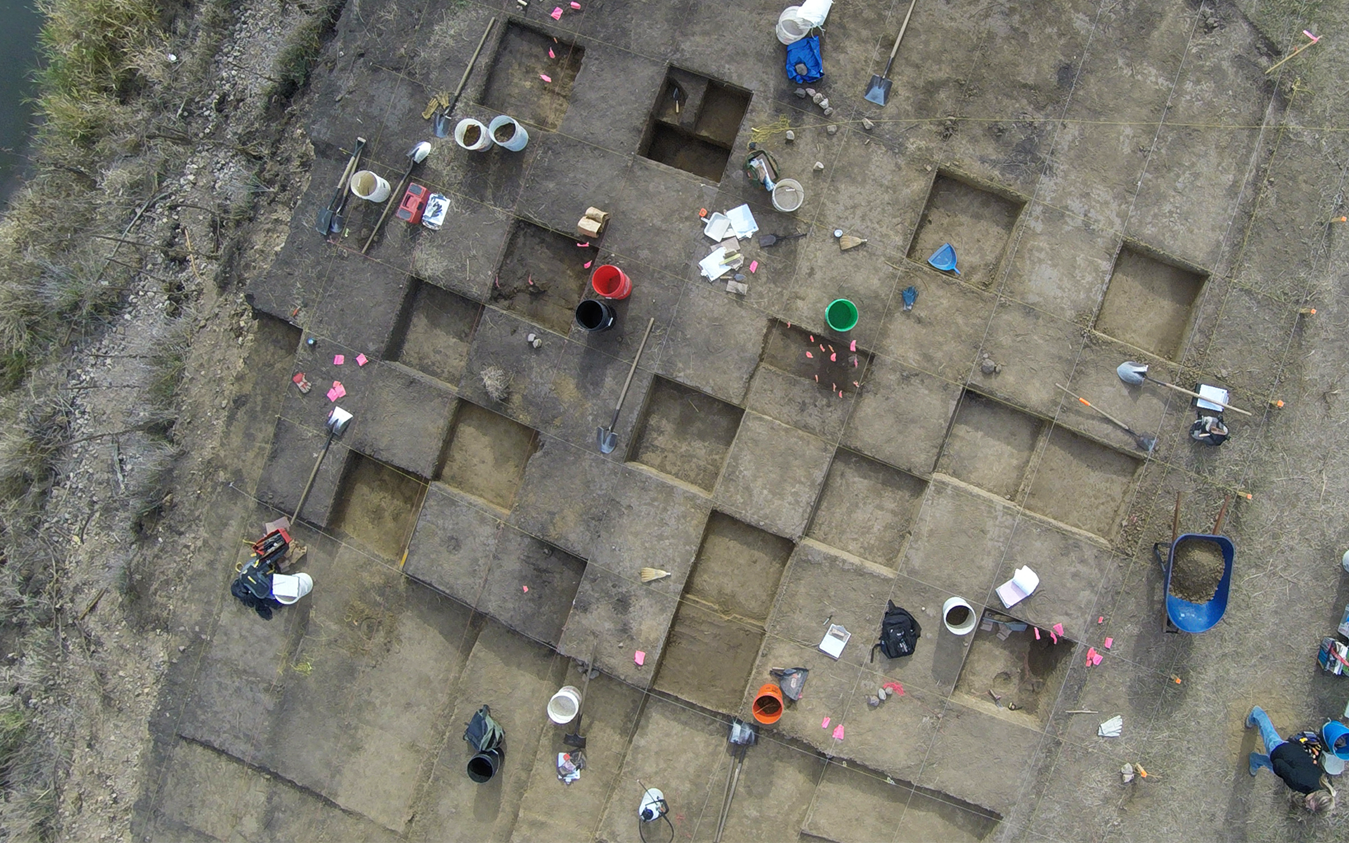 aerial image of an active archaeological excavation showing square units, tools, and people